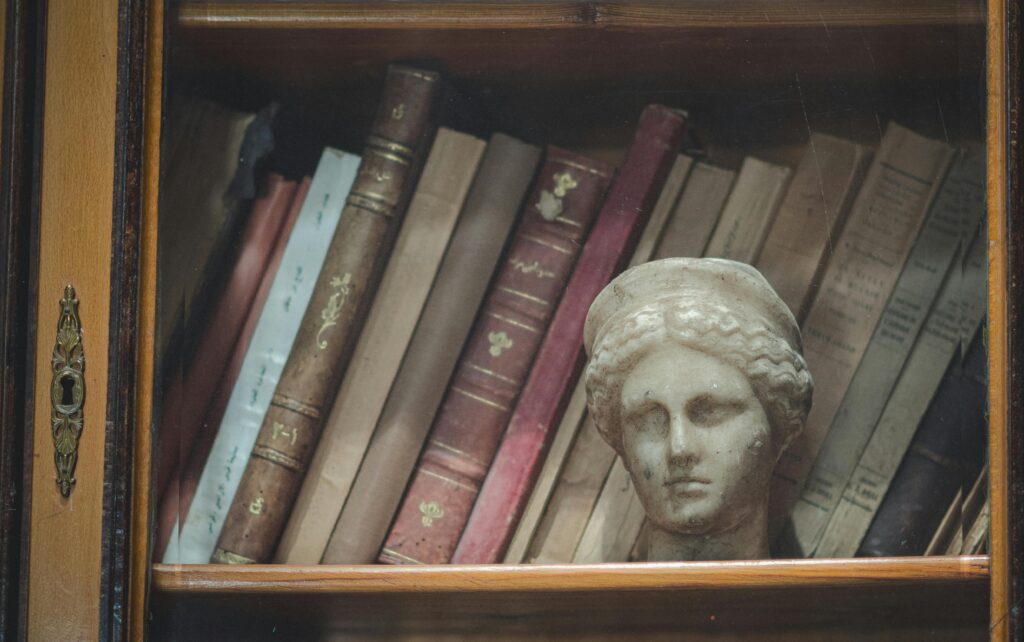 Close-up of antique books and a marble bust inside a vintage wooden bookshelf.